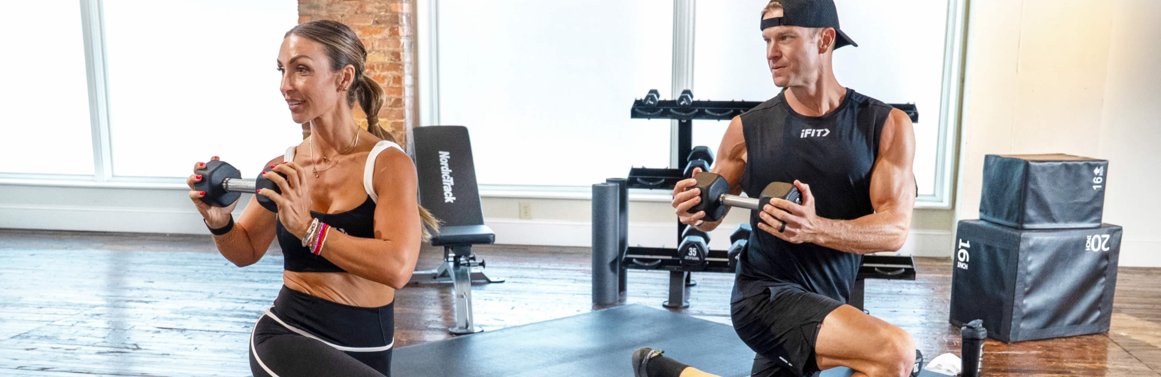 iFIT Trainers Bree Cox and John Peel do dumbbell lunges side by side in Transform 90, a 13-week strength program with 79 workouts.