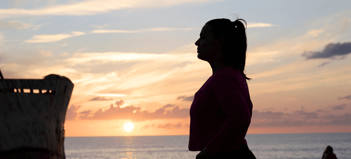 iFIT Trainer Erica Lugo captured in silhouette against a scenic sunrise during an outdoor walking and recovery session.